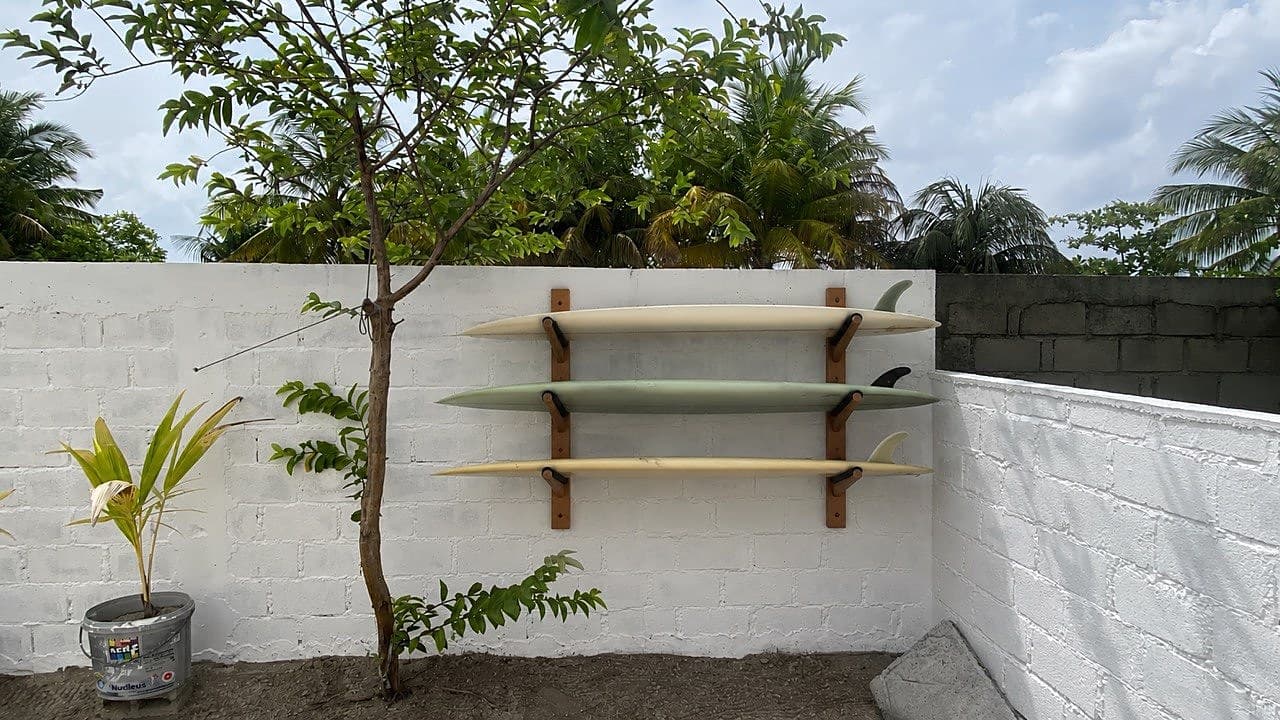 Three surfboards on a wooden wall rack against a whitewashed garden wall